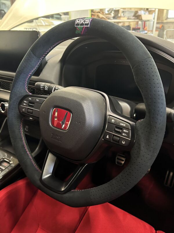 HKS replacement steering wheel for FL5 Type-S, black leather with red stitching and sporty design, shown from top angle.