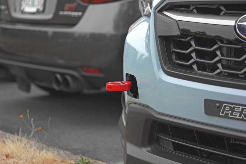 Red Perrin Performance tow hook kit for Subaru WRX, Crosstrek, OBXT, and Impreza front bumper, shown mounted on vehicle.