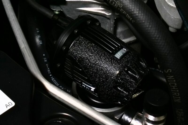 Black HKS SUPER SQV4 FL5 blow off valve installed on a car engine, showcasing its sleek design and branding.