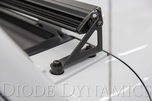 Diode Dynamics Jeep JL Wrangler/Gladiator hood bracket kit for light bars and cubes, shown installed on the vehicle's engine bay.