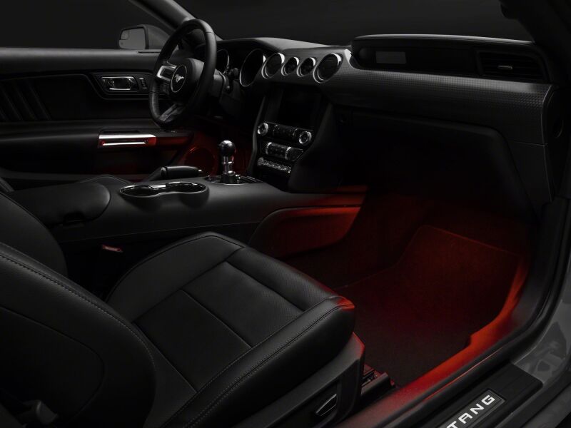 Raxiom LED footwell lighting kit in red installed inside a 2015-2023 Ford Mustang interior, illuminating the footwell area.