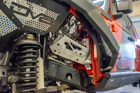 DV8 Offroad Jeep JL/JT engine bay compressor mount for air suspension, showing the durable black metal component installed in the engine bay.