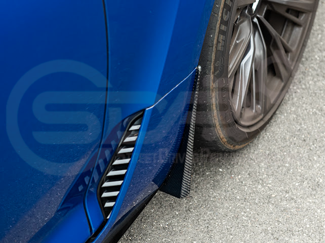Pair of black carbon fiber mud flaps for 2022-up Cadillac CT5-V Blackwing, with Street Driven Performance branding, mounted on vehicle.