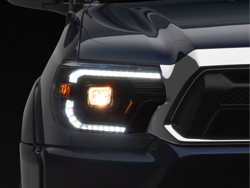 Raxiom black housing projector headlights with clear lens for 2012-2015 Toyota Tacoma, featuring switchback LED turn signals.