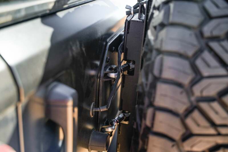 DV8 Offroad Jeep Wrangler JL MTO Series bumper spare tire swing gate tailgate accessory, showing the rugged bumper and tire mount.