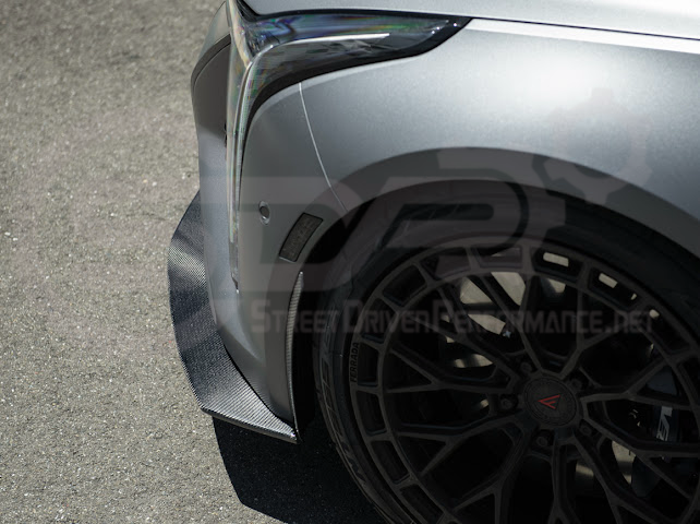 Cadillac CT5-V Blackwing factory OEM-style carbon fiber front lip splitter with ground effects and wheel arches, installed on the vehicle.