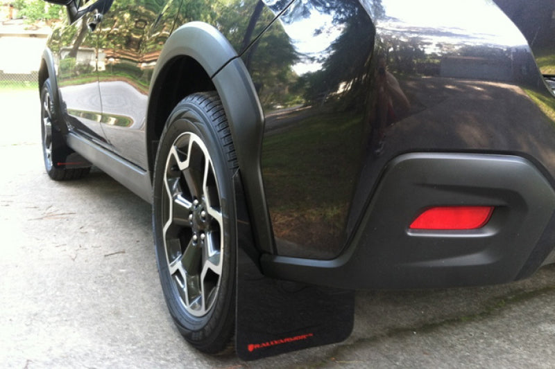 Rally Armor black mud flaps with orange logo installed on a 2013-2017 Subaru Crosstrek XV, showing durable rubber design and branding.