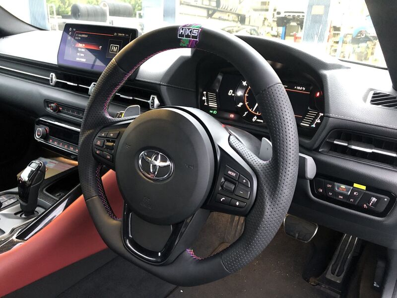 HKS GR Supra replacement steering wheel for A90 model, black with silver accents, showing the sporty design and textured grip.