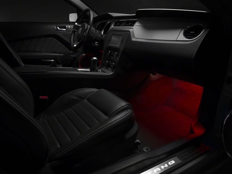 Raxiom Ford Mustang interior LED footwell lighting kit in red, illuminating the footwell area inside the vehicle.