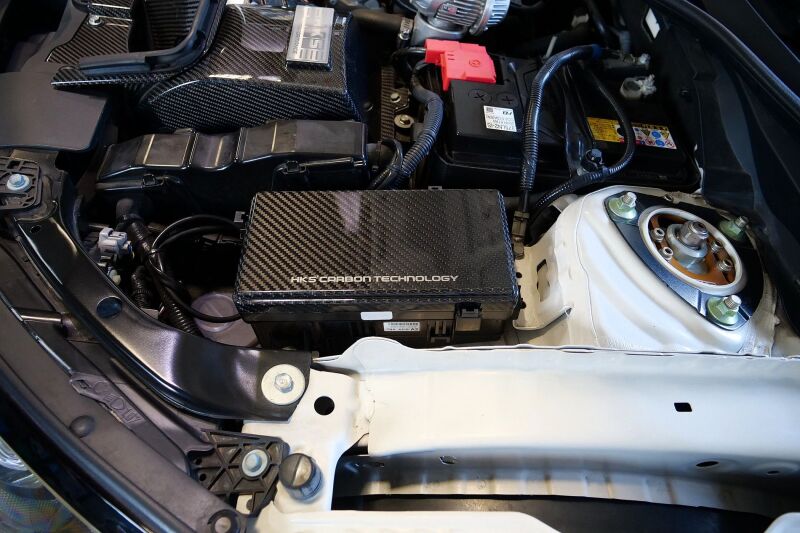 HKS dry carbon fiber fuse box cover for FK8 Honda Civic, showcasing sleek carbon accessories with a textured finish.