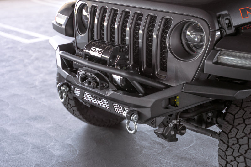 Steel front bumper by DV8 Offroad for Jeep Wrangler JK, JL, and Gladiator JT from 2018 to 2023, rugged off-road design with mounting points.